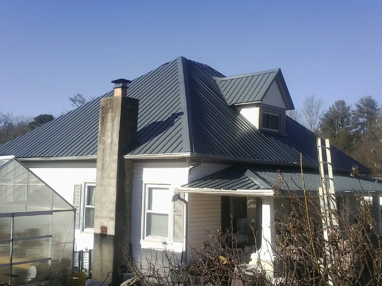 Dark blue standing seam metal roof on a white farmhouse with dormer — Slate & Tile Roof Repair by Roofing Brothers in Rosanky