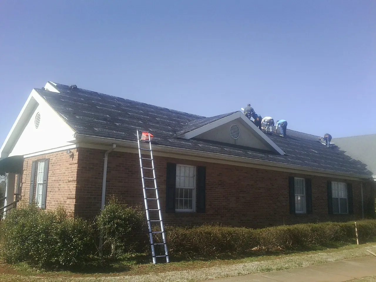 Crew tearing shingles off a brick ranch roof with a ladder set — Emergency Roof Repair work by our crew in Rosanky