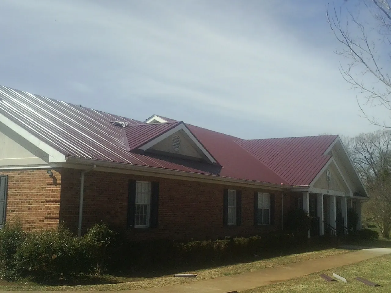 Red metal roof with gabled entries on a long brick building, from a Hail Damage Roof Repair job in Rosanky