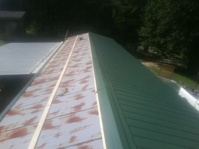 Old rusted panels beside newly installed green metal roofing — Wind Damage Roof Repair by Roofing Brothers in Rosanky