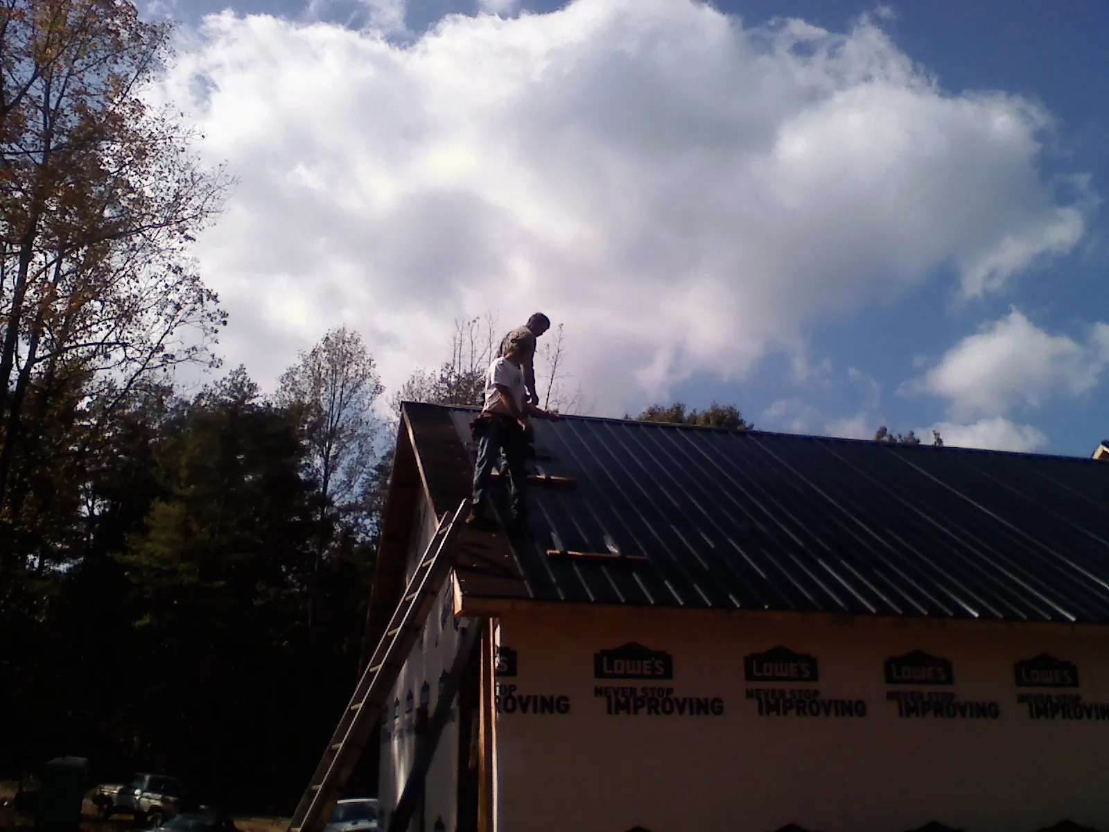Roofer fastening dark metal panels high against a cloudy sky, from a Roof Inspection job in Rosanky