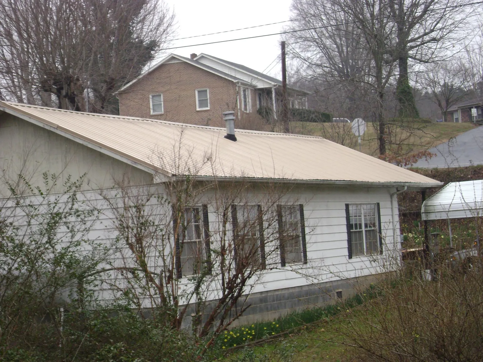 Tan metal roof on a white sided house set into a hillside — Commercial Roofing by Roofing Brothers in Rosanky