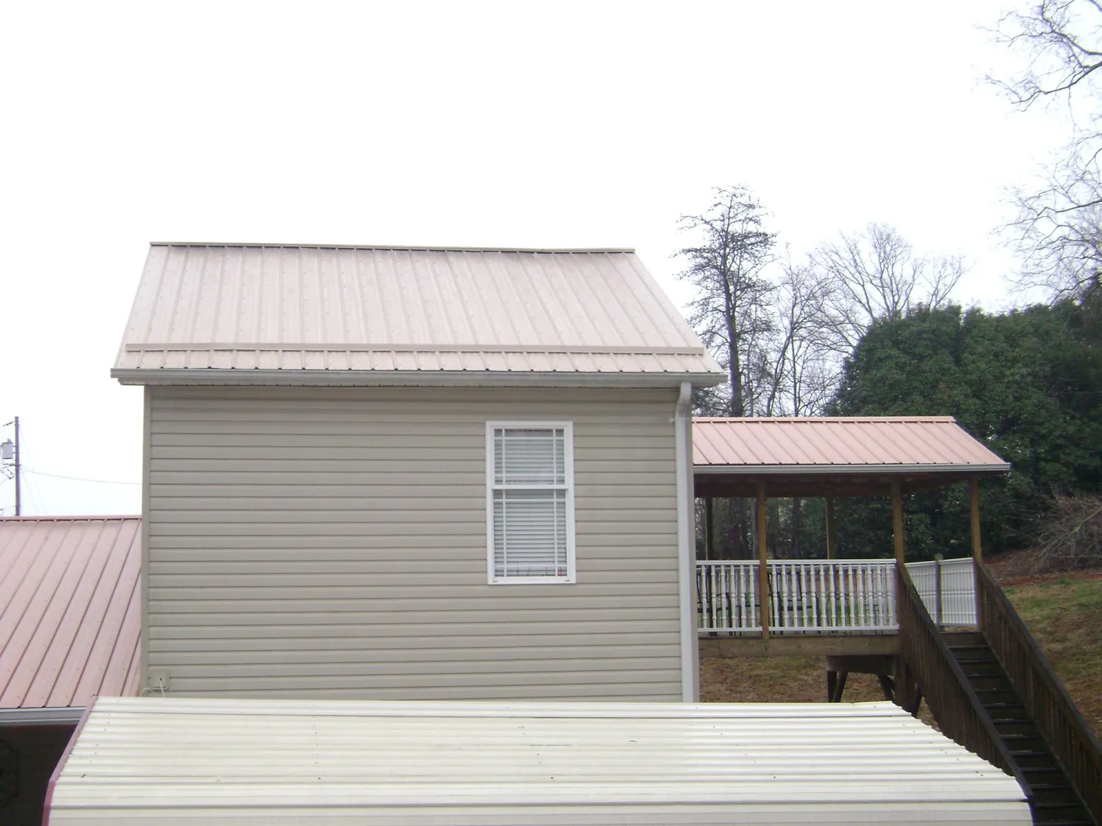 Tan metal roofs on a two story addition and attached porch, from a Roof Replacement job in Rosanky